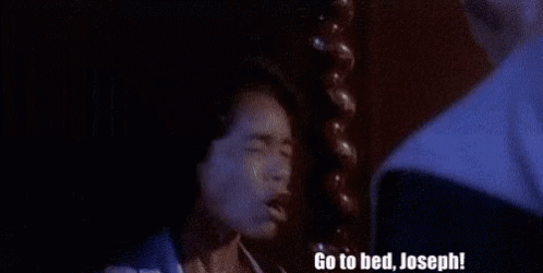 A Man Is Standing Next To A Woman In A Dark Room And Says `` Go To Bed , Joseph '' . GIF