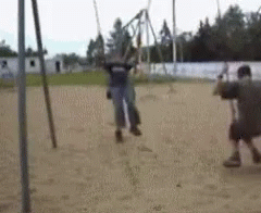 A Man Is Standing Next To A Woman On A Swing In A Playground . GIF