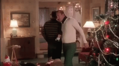 A Man Is Standing Next To Another Man In A Living Room With A Christmas Tree In The Background . GIF
