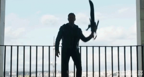 A Man Is Standing On A Balcony Holding A Large Sword In His Hand . GIF