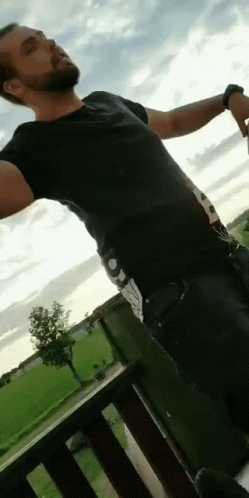 A Man Is Standing On A Balcony With His Arms Outstretched . GIF