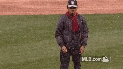 A Man Is Standing On A Baseball Field Wearing A Jacket And Hat . GIF