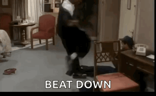 A Man Is Standing On A Chair In A Living Room With The Words `` Beat Down '' Written On The Screen . GIF