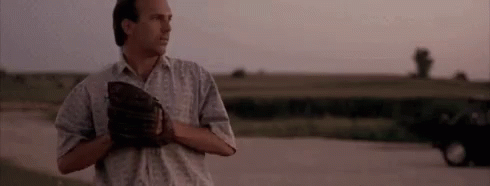 A Man Is Standing On A Dirt Road Holding A Baseball Mitt . GIF