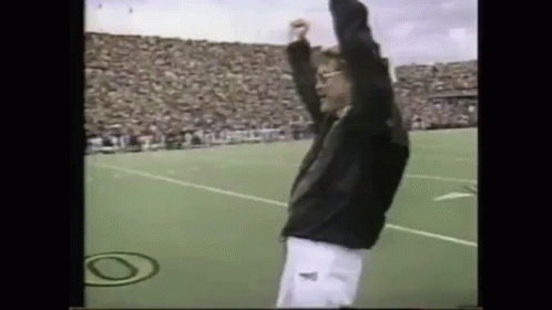A Man Is Standing On A Field With His Arms In The Air . GIF