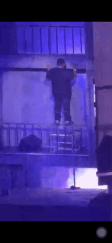 A Man Is Standing On A Ladder In A Dark Room With Blue Lights Behind Him . GIF