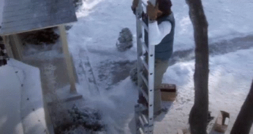 A Man Is Standing On A Ladder In The Snow Near A House . GIF