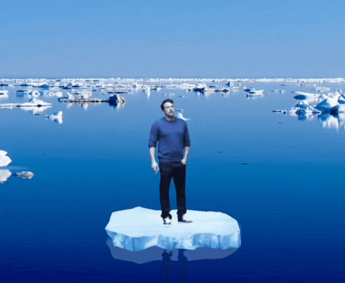 A Man Is Standing On A Piece Of Ice In The Middle Of The Ocean GIF