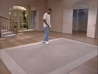 A Man Is Standing On A Rug In A Living Room With Stairs . GIF