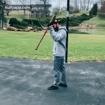 A Man Is Standing On A Sidewalk Holding A Cane And A Bat . GIF