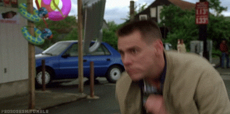A Man Is Standing On A Sidewalk In Front Of A Blue Car And Talking On A Cell Phone . GIF