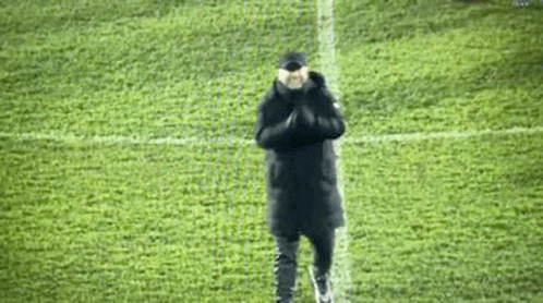 A Man Is Standing On A Soccer Field With His Hands Folded In Front Of Him . GIF