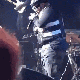 A Man Is Standing On A Stage Holding A Microphone And A Trumpet . GIF