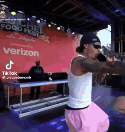 A Man Is Standing On A Stage Holding A Microphone In Front Of A Sign That Says Verizon . GIF