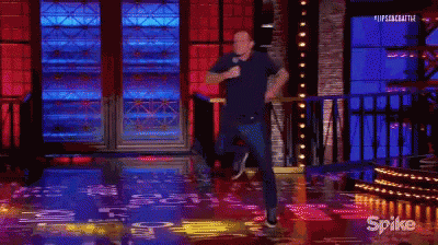 A Man Is Standing On A Stage Holding A Microphone While Dancing . GIF