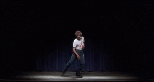 A Man Is Standing On A Stage In Front Of A Blue Curtain And Dancing . GIF