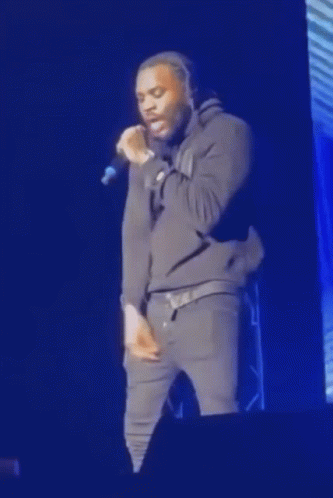 A Man Is Standing On A Stage Singing Into A Microphone . GIF