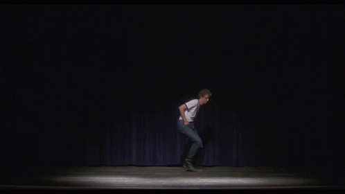 A Man Is Standing On A Stage With His Arms Outstretched And A Blue Curtain Behind Him . GIF