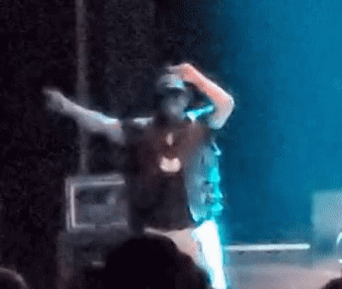 A Man Is Standing On A Stage With His Arms Outstretched And A Microphone In His Hand . GIF