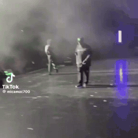 A Man Is Standing On A Stage With Smoke Coming Out Of It And A Tiktok Logo In The Corner . GIF