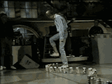 A Man Is Standing On A Table With A Bunch Of Bottles On It GIF