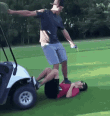 A Man Is Standing On Another Man 'S Back In A Golf Cart On A Golf Course . GIF