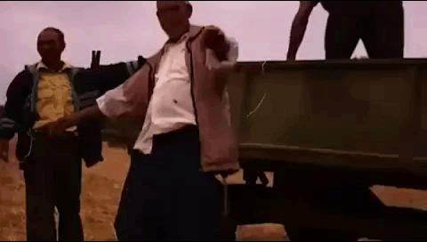 A Man Is Standing On The Back Of A Truck While Another Man Stands Behind Him . GIF