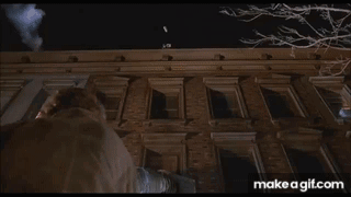 A Man Is Standing On The Roof Of A Tall Building At Night . GIF