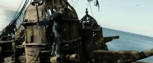 A Man Is Standing On The Side Of A Wooden Ship In The Ocean . GIF