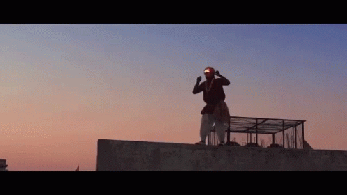 A Man Is Standing On Top Of A Building With His Arms In The Air . GIF
