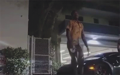 A Man Is Standing On Top Of A Car In Front Of A Building At Night . GIF