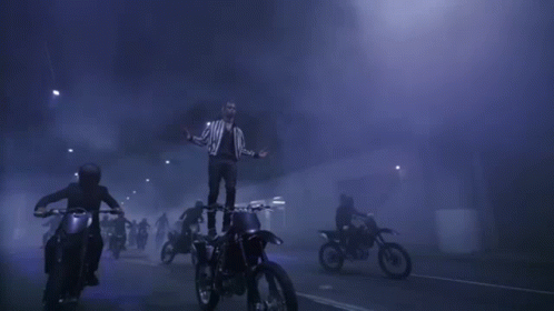 A Man Is Standing On Top Of A Dirt Bike In The Middle Of A Crowd Of People Riding Motorcycles . GIF