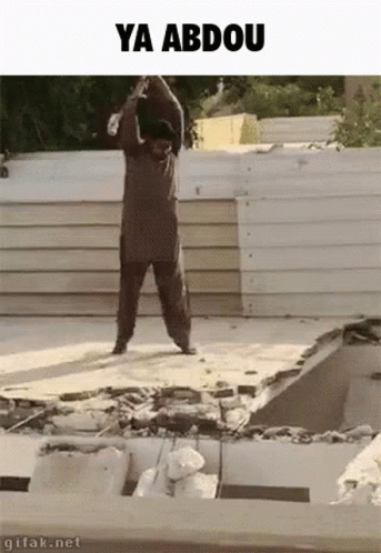A Man Is Standing On Top Of A Pile Of Concrete With The Words Ya Abdou Written Above Him . GIF