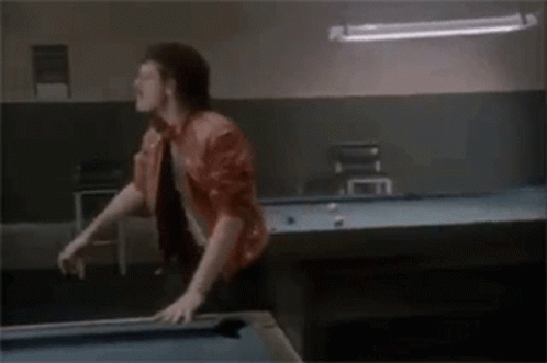 A Man Is Standing On Top Of A Pool Table In A Pool Hall . GIF