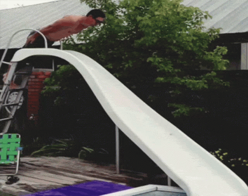 A Man Is Standing On Top Of A Slide Looking Down GIF