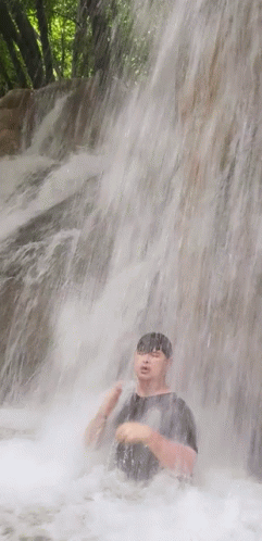 A Man Is Standing Under A Waterfall With His Head In The Water GIF