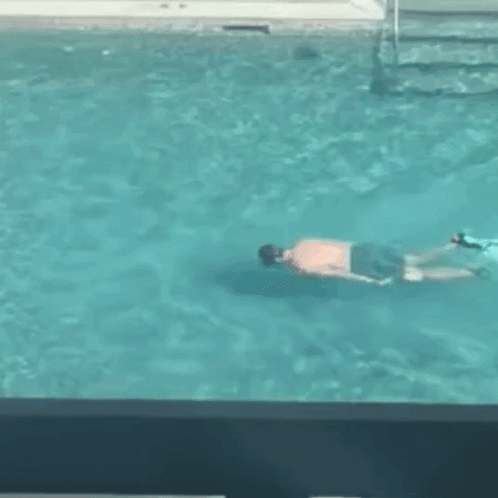 A Man Is Swimming In A Swimming Pool While Another Man Watches . GIF