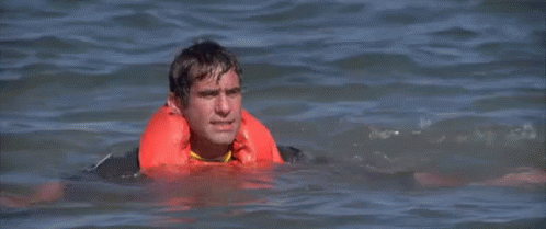 A Man Is Swimming In The Ocean Wearing A Life Jacket . GIF