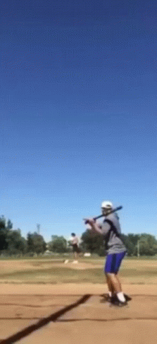 A Man Is Swinging A Bat At A Ball In A Field GIF