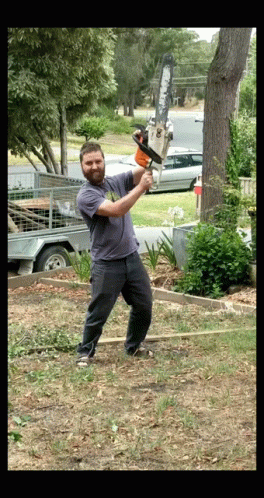 A Man Is Swinging A Chainsaw At A Tree Trunk GIF
