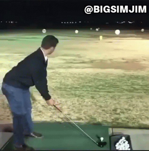 A Man Is Swinging A Golf Club At A Golf Ball On A Golf Course . GIF