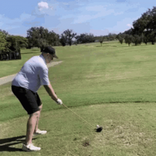 A Man Is Swinging A Golf Club At A Golf Ball On A Golf Course GIF
