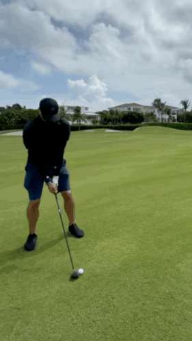 A Man Is Swinging A Golf Club At A Golf Ball On A Golf Course GIF