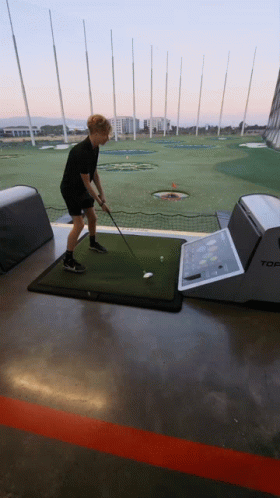 A Man Is Swinging A Golf Club At A Golf Ball On A Mat That Says Top GIF