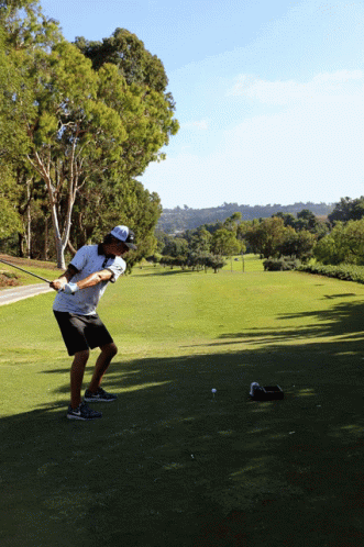 A Man Is Swinging A Golf Club At A Golf Ball GIF
