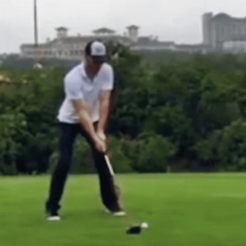 A Man Is Swinging A Golf Club At A Golf Ball . GIF