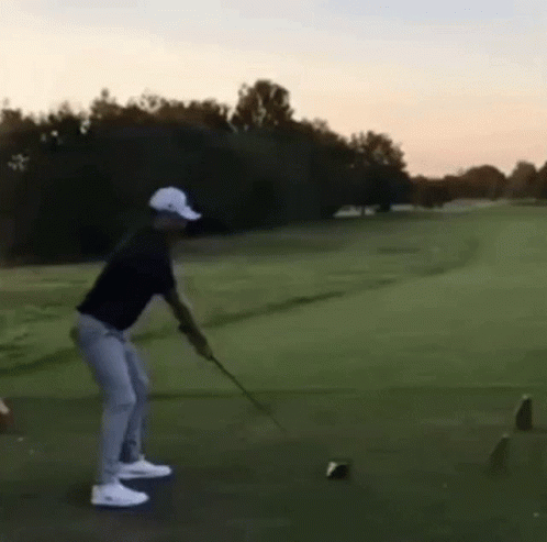A Man Is Swinging A Golf Club On A Golf Course And Hitting A Ball . GIF