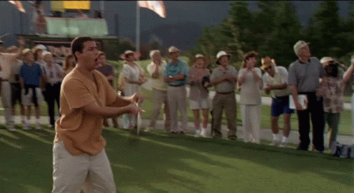 A Man Is Swinging A Golf Club On A Golf Course While A Crowd Watches GIF