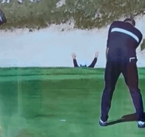 A Man Is Swinging A Golf Club On A Golf Course While Another Man Watches GIF