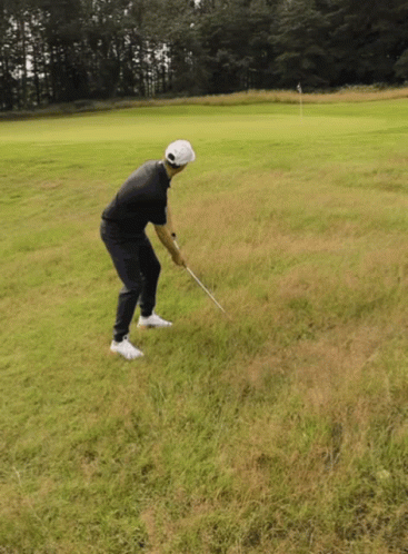 A Man Is Swinging A Golf Club On A Grassy Field GIF